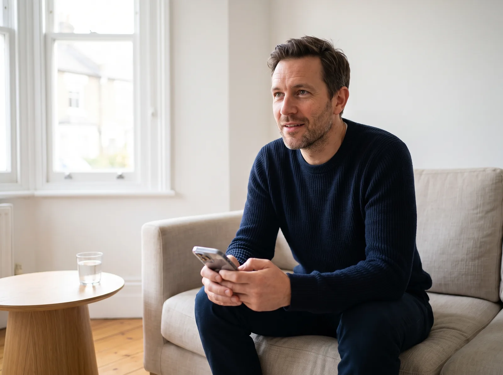 Mann um vierzig auf einem hellen Sofa zu Hause, liest auf dem Smartphone ein Gesundheitsprogramm